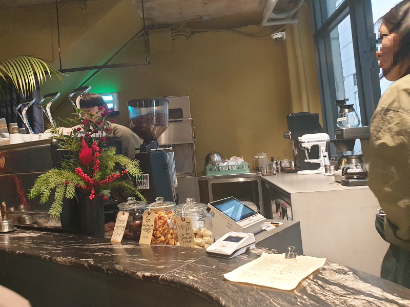 테이블 너머 직원과 바리스타가 보인다. 테이블에는 메뉴판이 놓여있다.