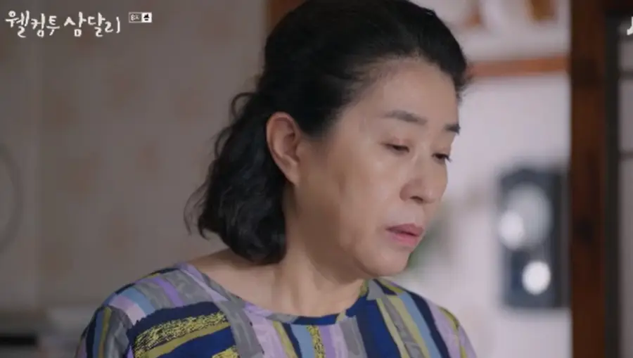 웰컴투삼달리- 파란색과 연두색 줄무늬옷을 입고 땅을 쳐다보는 엄마 고미자