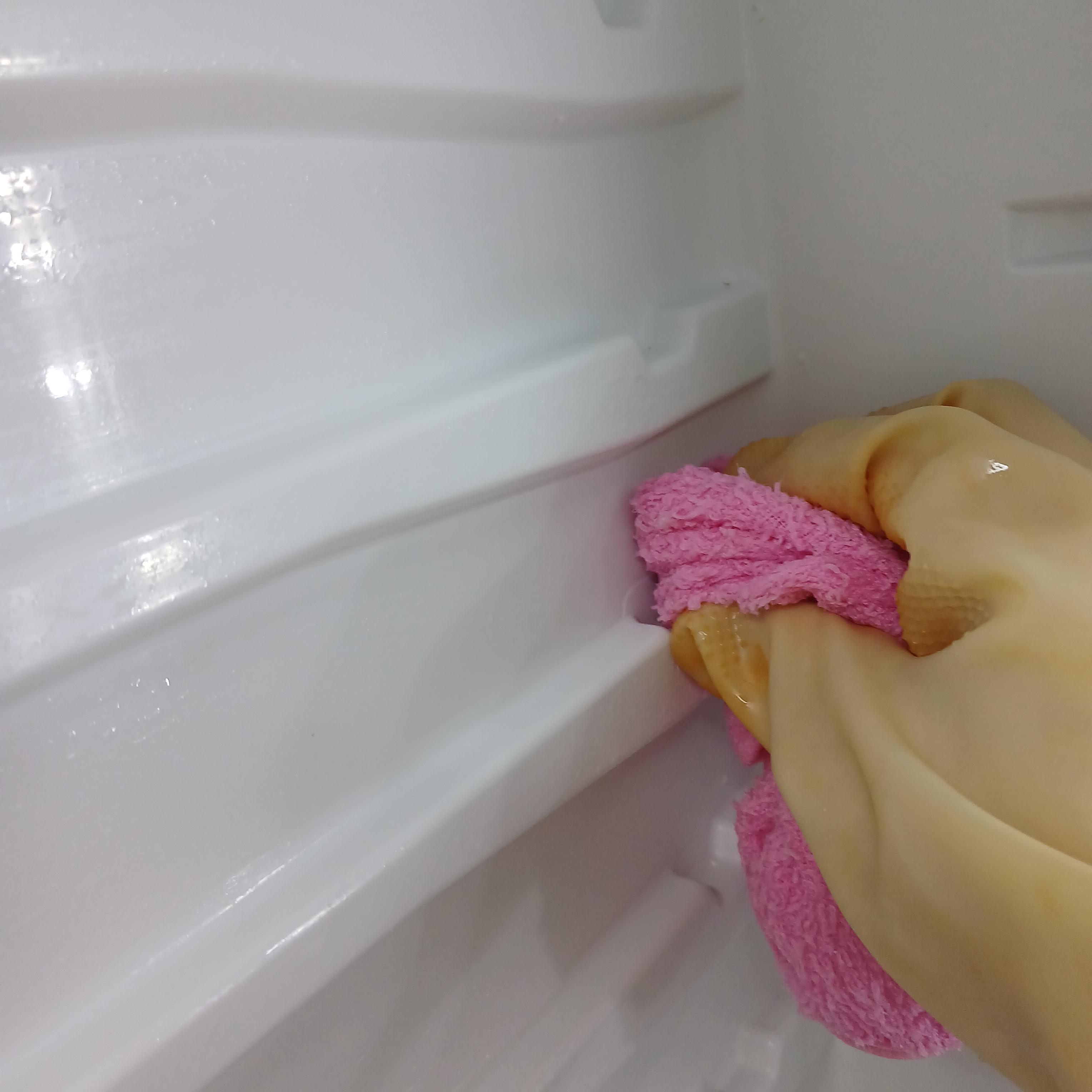 고무장갑을 낀 손으로 분홍색 행주로 냉장고 내부의 묵은 때를 닦아내는 모습