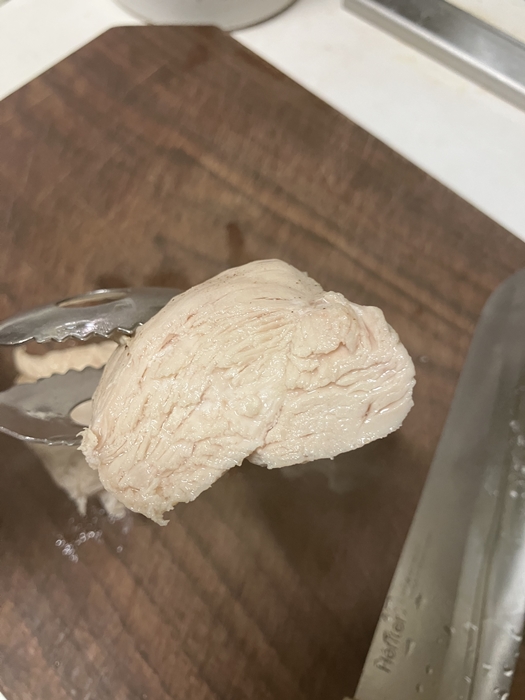 집게로 들어 올린 닭가슴살 단면, 결 사이사이로 촉촉하게 익은 속살이 보이는 모습