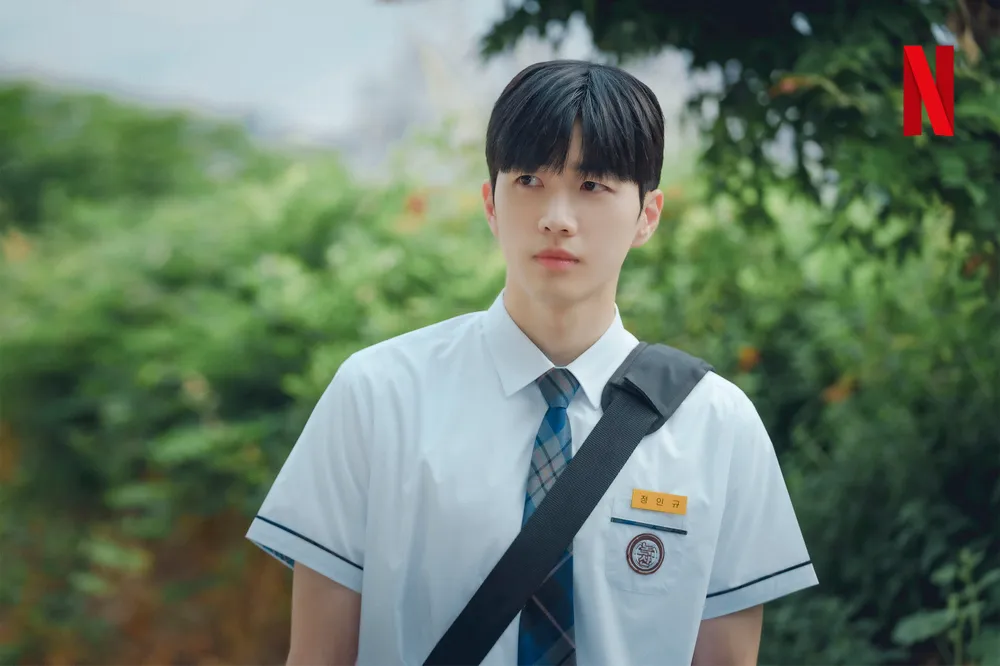 어느 풀숲을 배경으로 여름 반팔 교복에 크로스 백을 메고 서 있는 드라마 너의 시간 속으로의 정인규 캐릭터