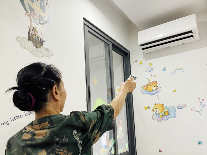 베트남 어머니는 전기 사용량을 줄이기 위해 에어컨을 리모컨으로 끄고 있습니다.