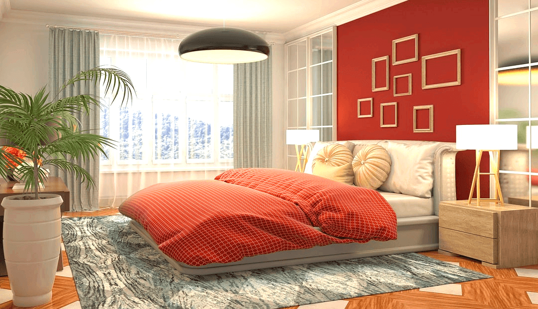 침실 풍경이다. 주황색 이불이 침대에 있고 창가엔 화사한 하얀 커튼이 있다. 커다란 하얀 화분에 녹색 식물이 자란다.