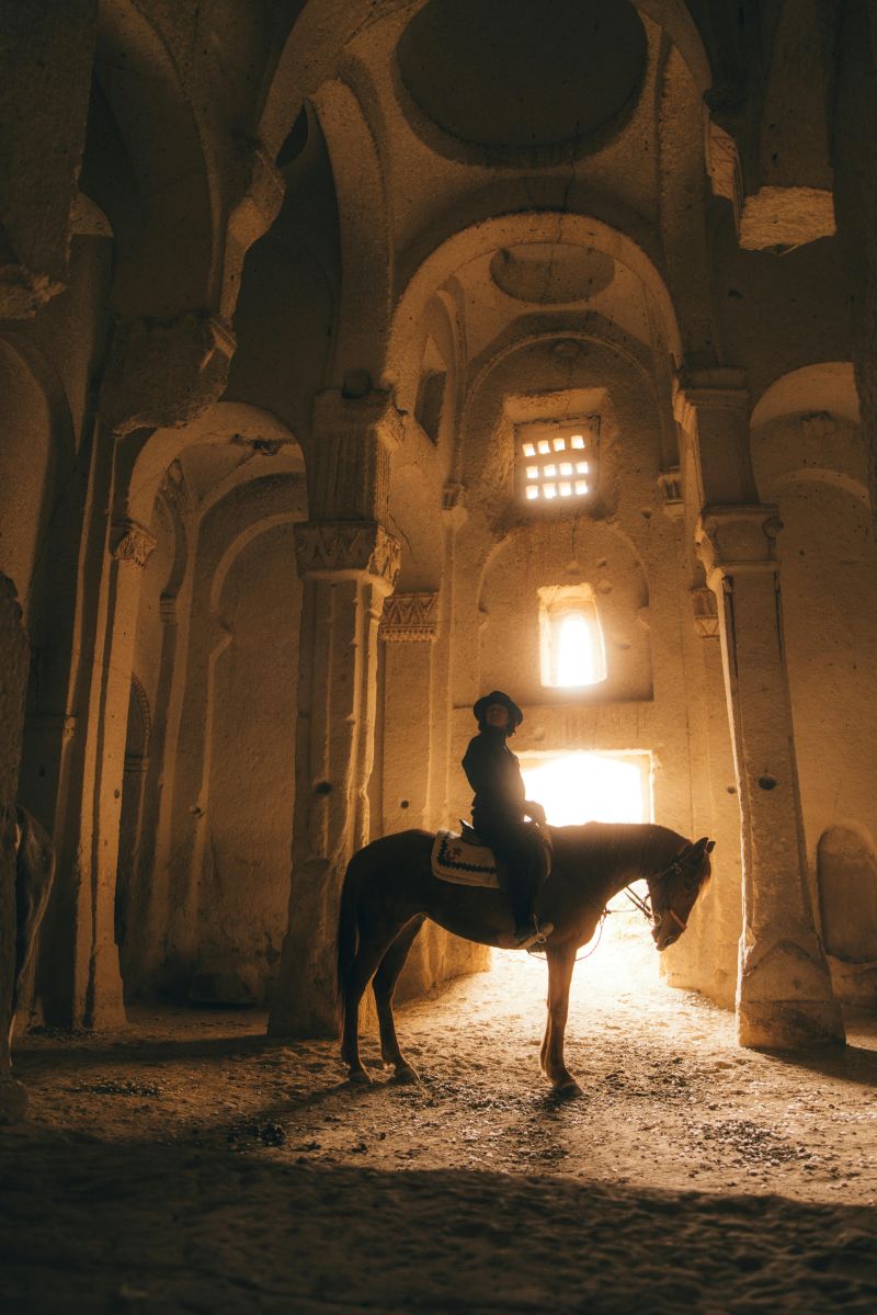 카파도키아 동굴 내부 아치형 기둥 사이에서 말을 타고 천천히 이동하는 체험자 모습