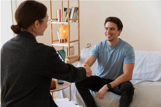 편안한 상담실에서 전문가와 웃으며 악수하는 젊은 남성. 심리상담 시작을 앞둔 따뜻한 분위기의 장면.