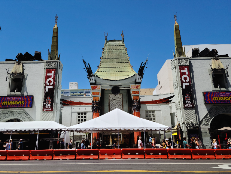 차이니즈 시어터를 길 건너편에서 찍은 사진. 영화관 앞에 큰 천막이 쳐져 있고 거리를 통제하는 가드레일이 세워져 있다. 영화관의 양쪽 벽에는 미니언즈 영화를 홍보하는 포스터가 걸려있다.