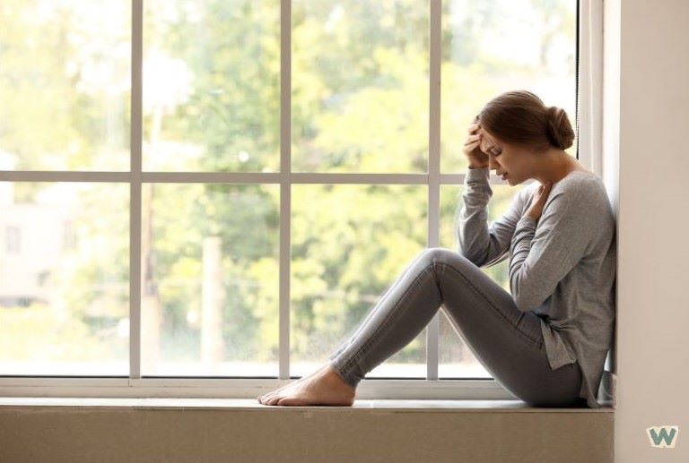 중년 여성이 창가에 앉아 머리를 감싸고 불안감과 스트레스를 느끼는 모습, 공황장애 증상을 표현하는 이미지 via canva