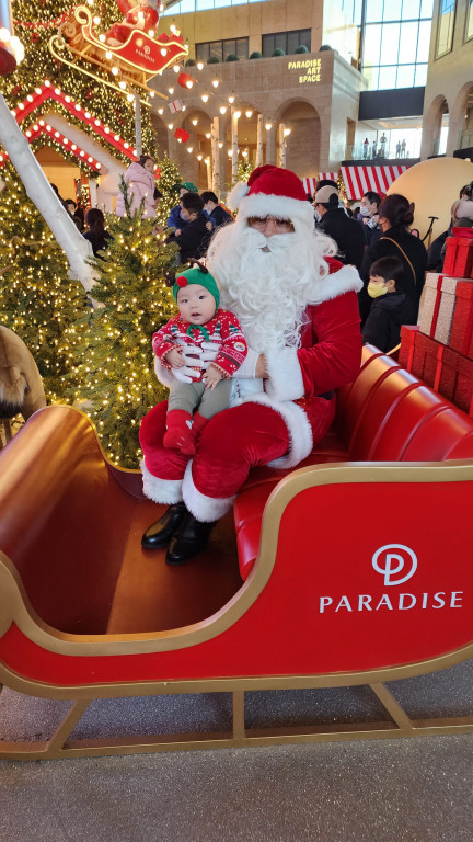 인천 파라다이스 시티에서 산타클로스와 함께 사진을 찍고 있는 아기 모습. 크리스마스 의상과 루돌프 모자를 쓴 아이가 귀엽게 포즈를 취하고 있는 모습