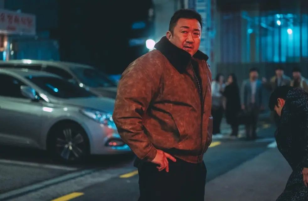 범죄도시-밤거리 갈색 가죽점퍼 검은바지입고 허리춤에 팔을 얹은 마동석