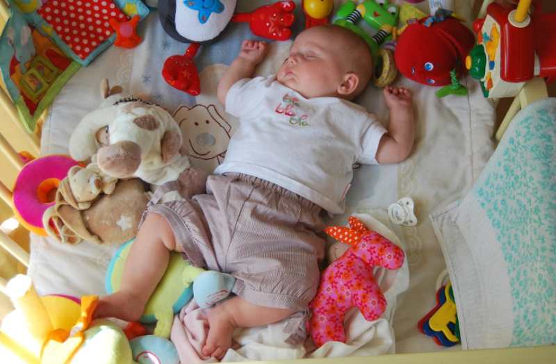 다양한 장난감과 함께 침대에서 잠든 아기, 육아용품 렌탈과 구독 서비스를 상징하는 장면