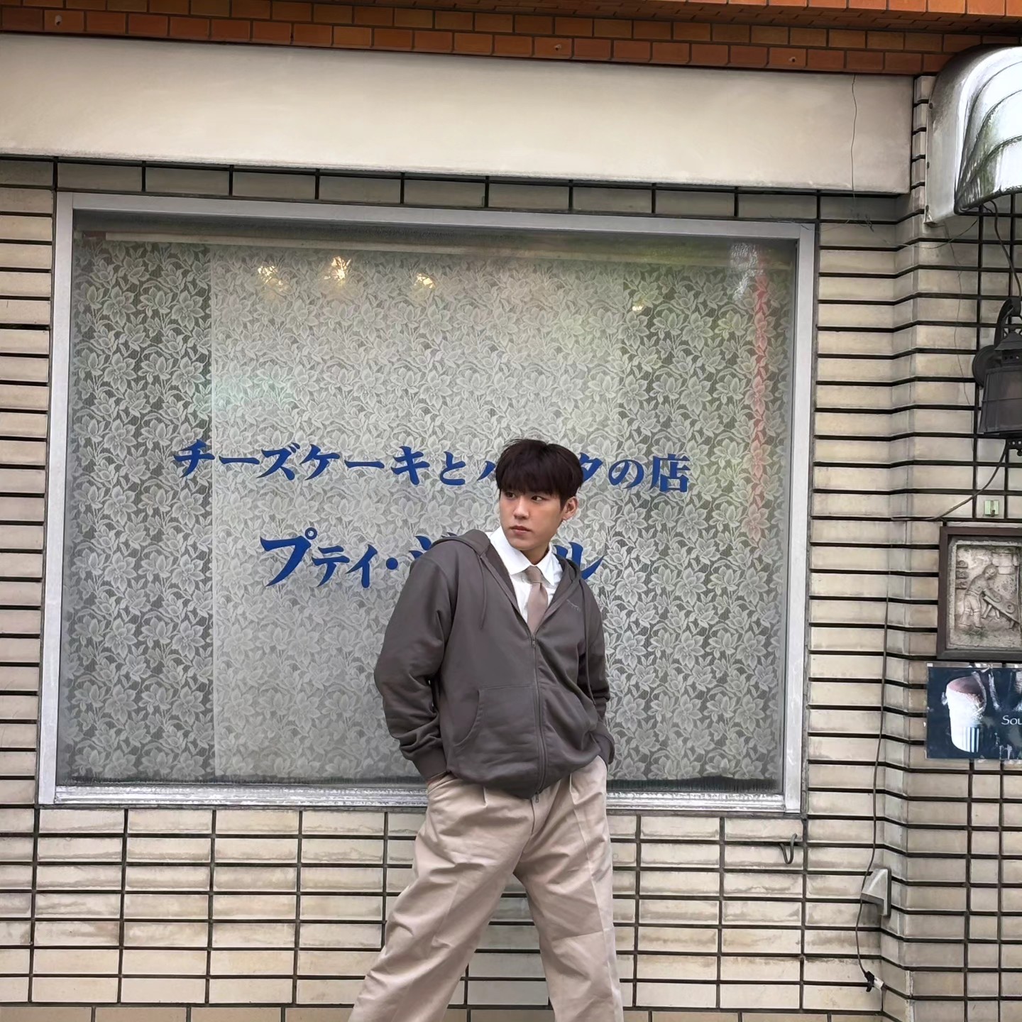 일본의 어느 거리에서 흰 셔츠, 브라운 넥타이, 후드 집업, 와이드 브라운 진을 입고 포즈를 취한고 있는 워너원 박우진의 사진