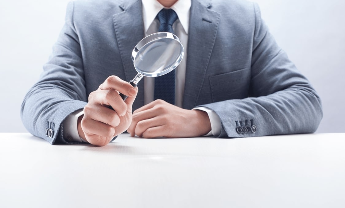 책상에서 돋보기를 들고 있는 남성의 상반신 모습