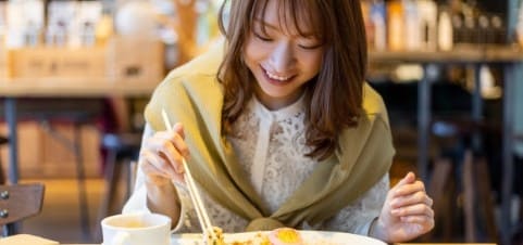 여성이 식당안에서 젓가락을 들고 음식을 보고 있다.