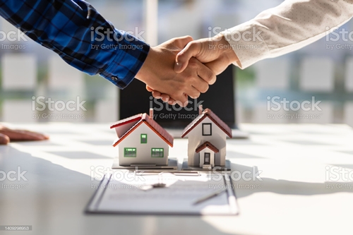 주택모형 위에서 두 남자가 악수하고 있는 사진