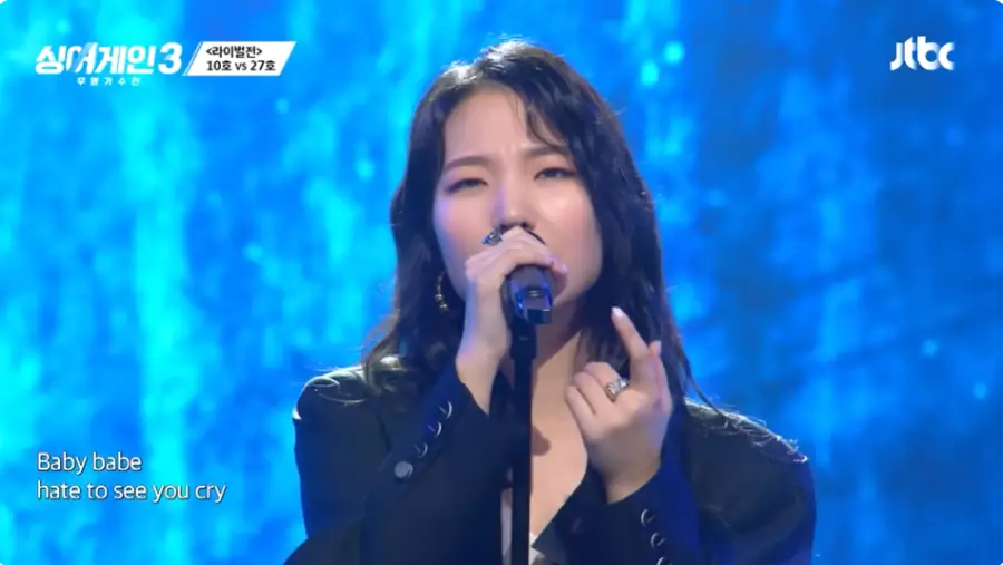 싱어게인3-
파란무대배경 검은쟈켓 긴웨이브머리 스탠딩마이크를 잡고 노래하는 27호