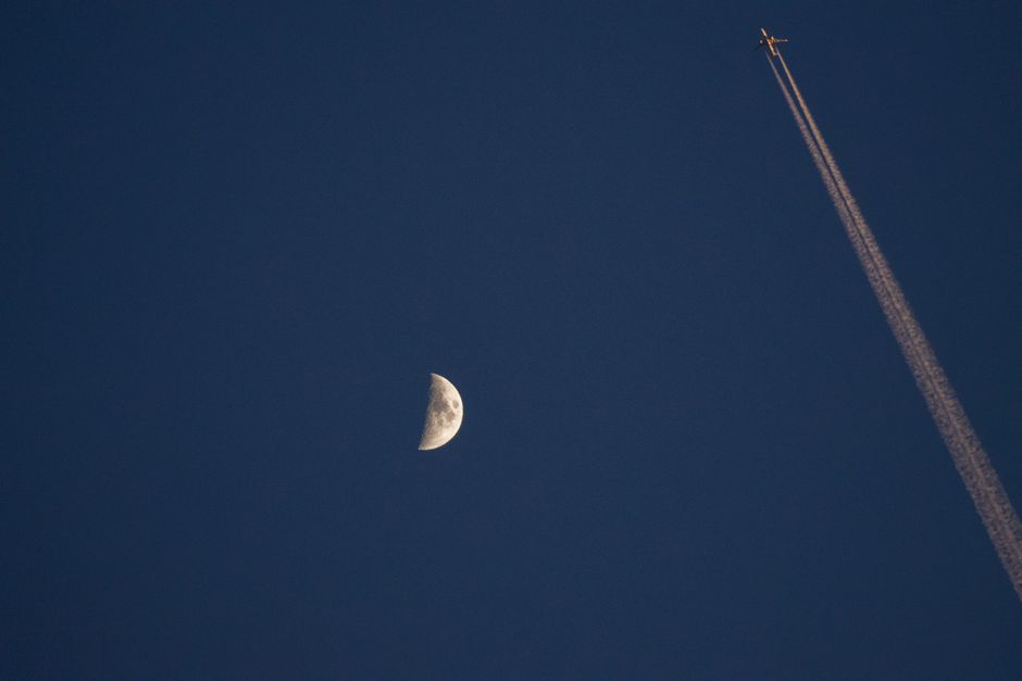 Airplane with contrail passing near the moon against a deep blue night sky, captured over J&ouml;nk&ouml;ping.