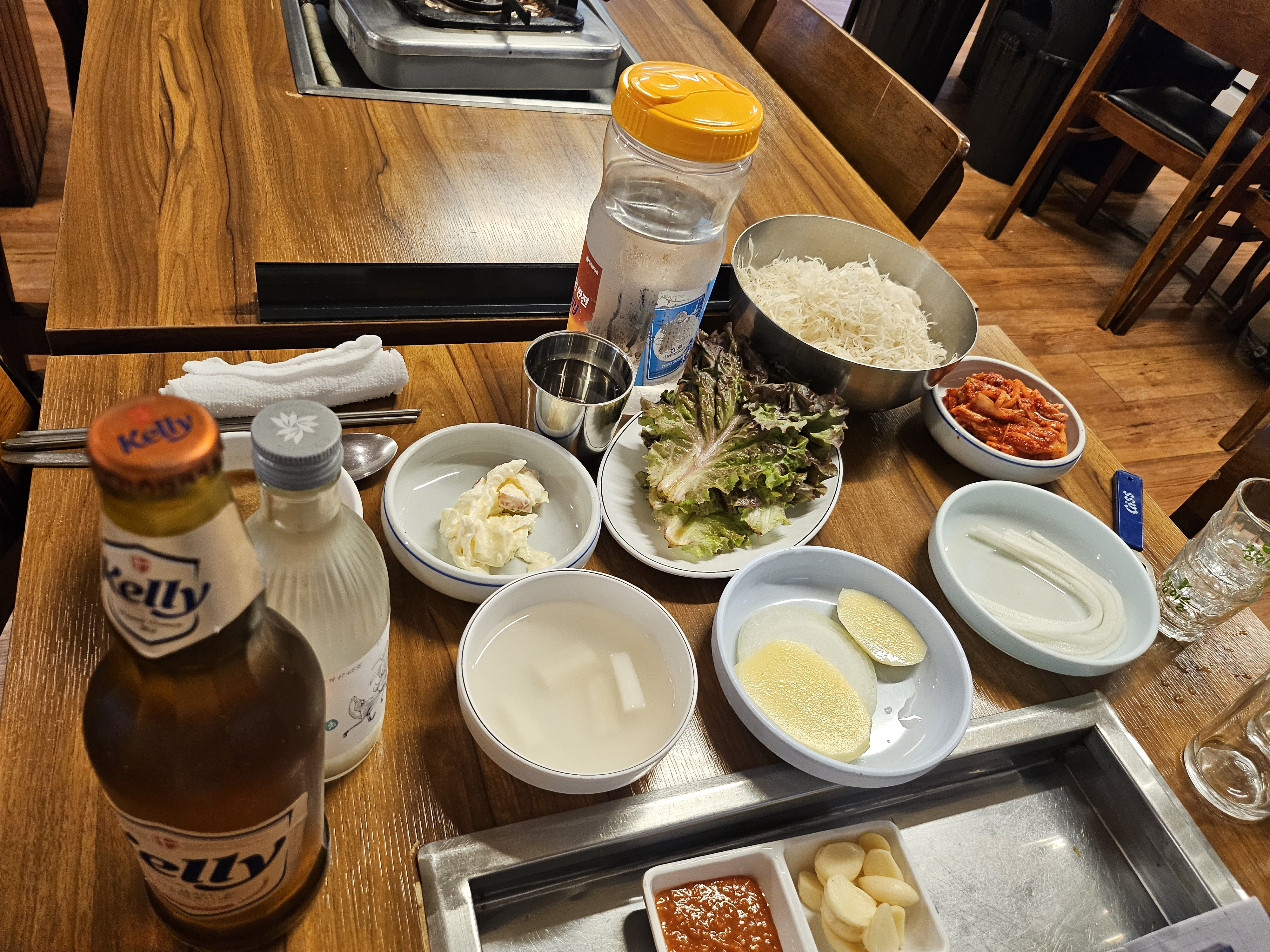 테이블에 놓인 다양한 밑반찬과 쌈 채소, 맥주병과 소주병