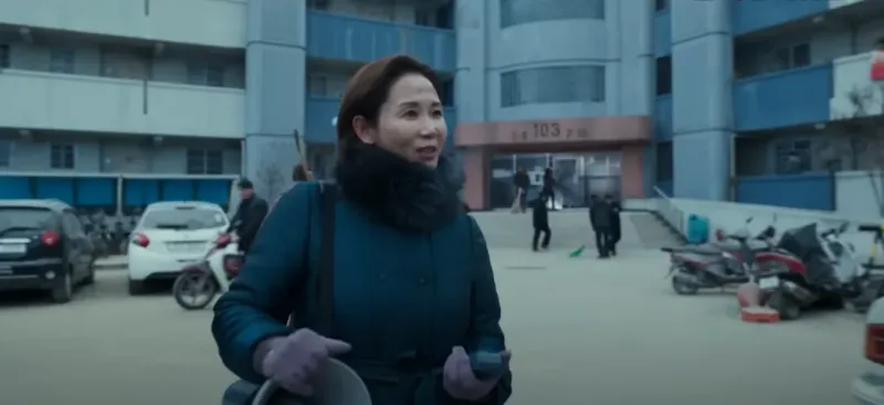 황궁아파트 입구를 배경으로 남색 겨울 코트를 입고 어깨엔 메가폰을 한손엔 메가폰 확성기를 쥐고 누군가에 말을 걸고 있는 김선영