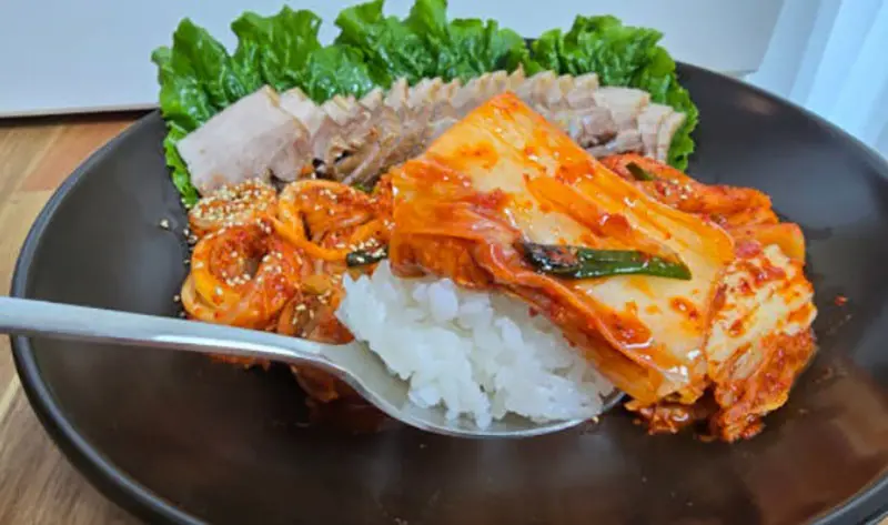 돼지고기 수육과 맛있는 배추김치가 흰 쌀밥 위에 놓여 있는 이미지.