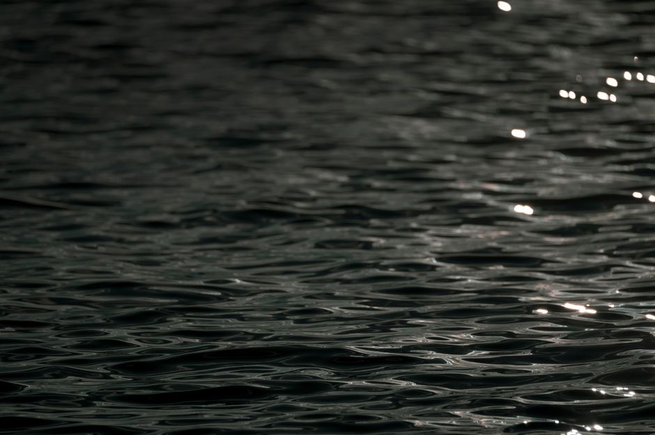 Dark ocean water with gentle ripples reflecting soft light, creating a serene and moody scene.