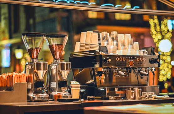 커피숍 풍경이다. 원두커피머신이 있고 하얀 종이컵들이 가득 쌓여있다.