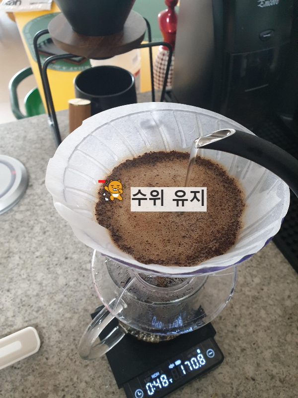 드리퍼 안에 붉은 수위 표시와 '스위 유지'라는 글자가 써있다. 드리퍼로 물을 가늘게 붓는 중