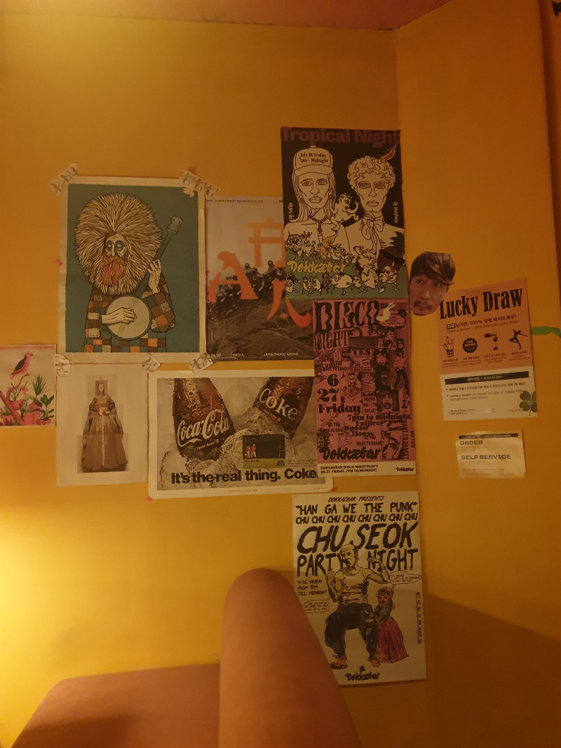 노란색 벽면에 다양한 그림과 포스터들이 부착되어 있다.