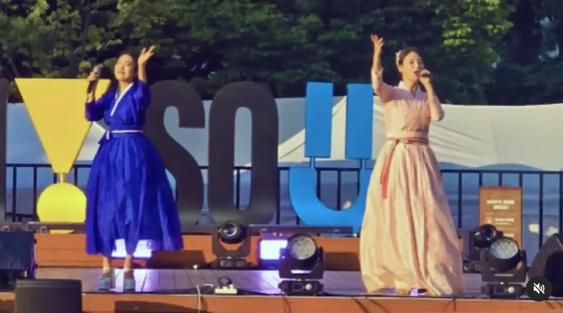 한복을 입은 두 여성 아티스트가 서울광장 무대에서 전통 음악 공연을 펼치며 손을 들어 관객과 호흡하는 순간