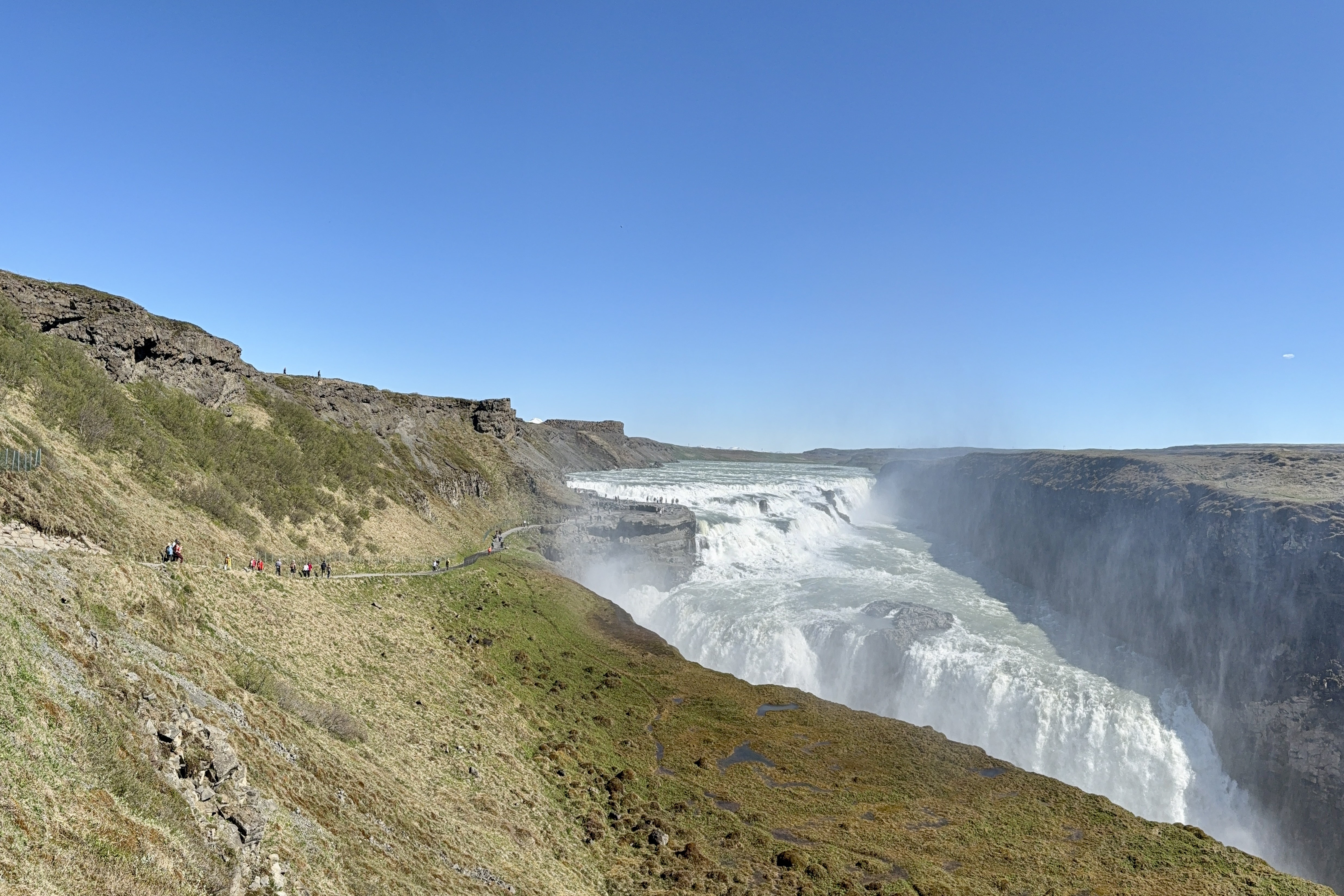 아이슬란드 굴포스 폭포의 웅장한 물줄기와 협곡 전경, 관광객들이 물안개를 따라 산책로를 걷는 모습.