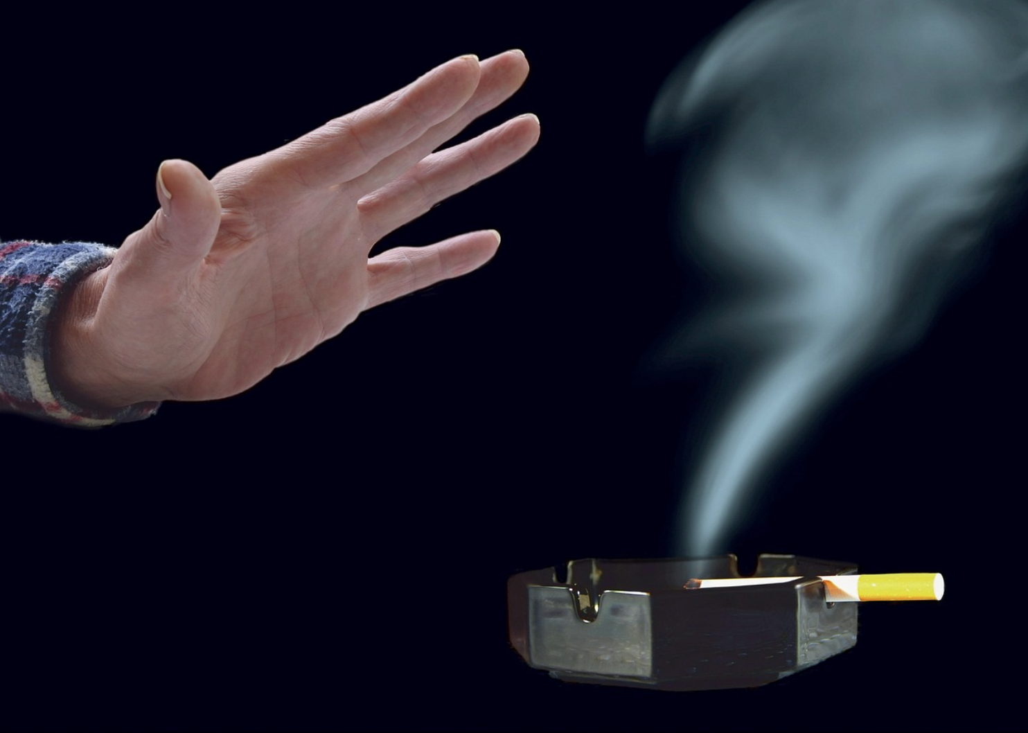 담배 연기가 나는 재떨이 앞에서 손으로 연기를 피하는 모습