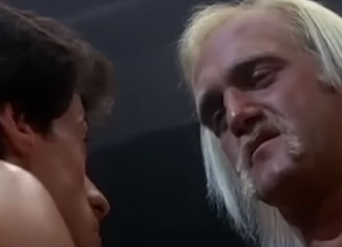 영화 ‘록키 3’ 속 한 장면으로, 헐크 호건이 실베스터 스탤론을 강렬한 눈빛으로 바라보고 있는 순간. 긴 금발 머리와 클래식한 외모가 강조된다.