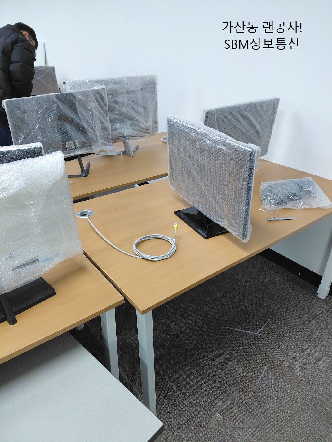 랩으로 감싸진 새 모니터들과 배선이 되지 않은 깨끗한 책상 상판의 대조적인 모습