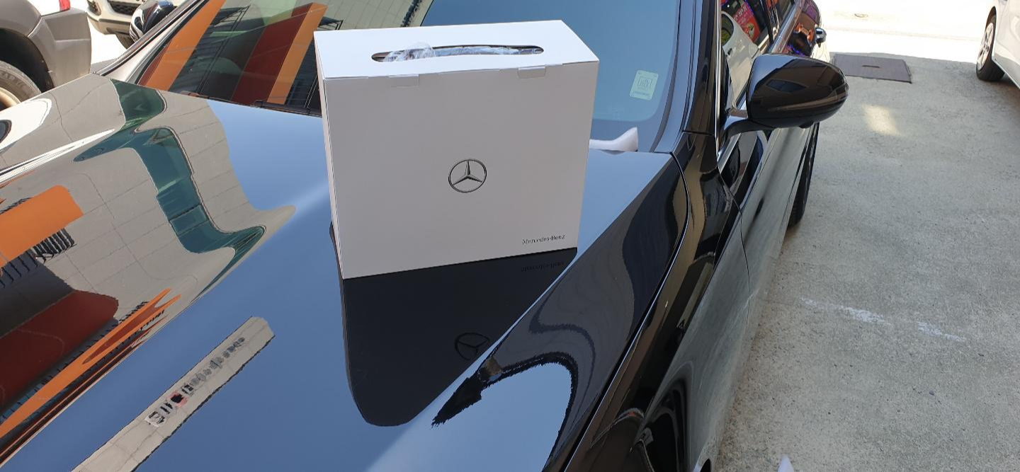벤츠 차량 위에 올려진 화이트 박스형 사은품, 전면에 벤츠 로고 인쇄