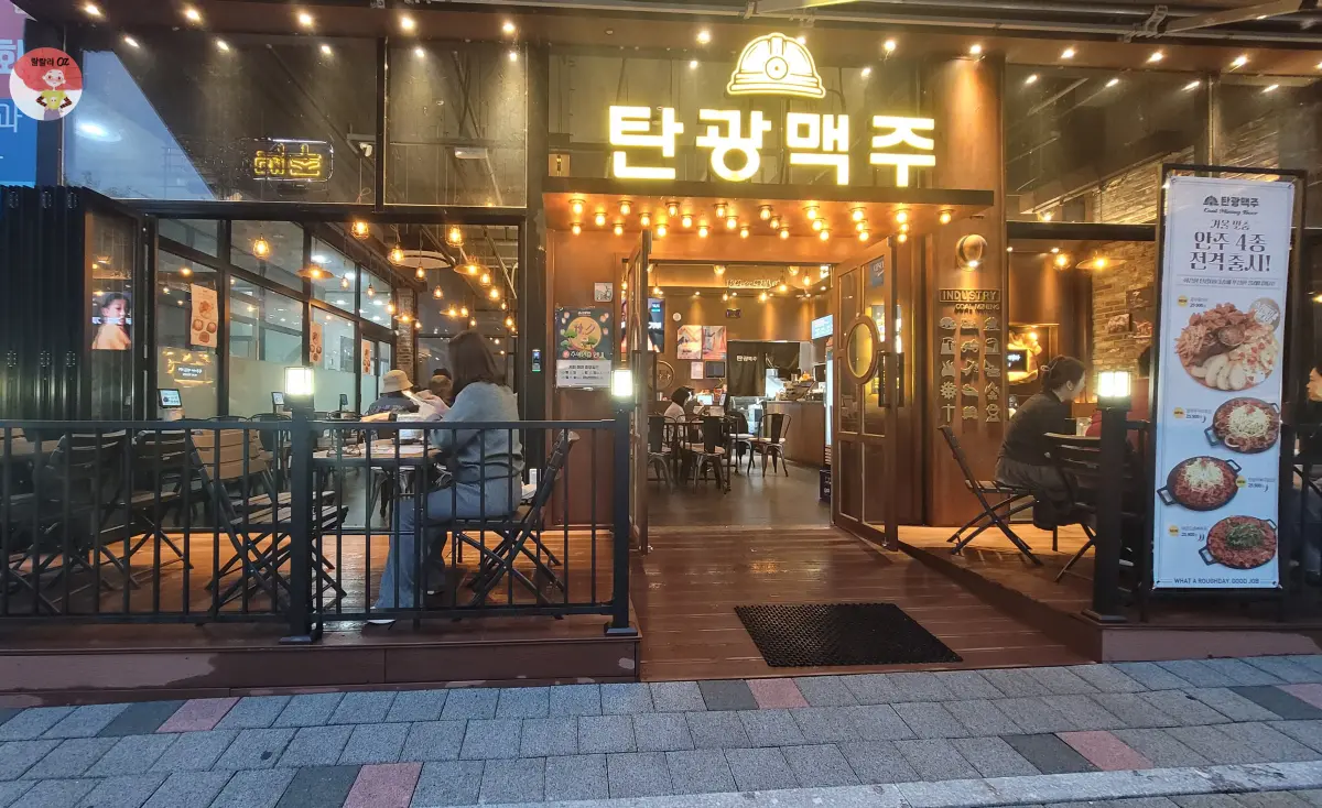 경기-남양주시-다산동-탄광맥주-노란색-간판-불빛-아래-테라스에-앉아서-술과-안주를-즐기는-사람들