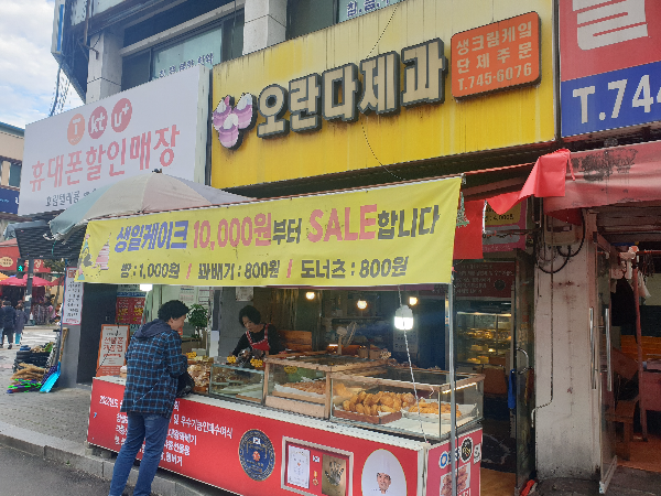 노란 간판에 오란다 제과라는 간판이 보인다. 붉은 색 테이블 위에 판매되는 빵이 유리 쇼케이스 안에 들어 있다.