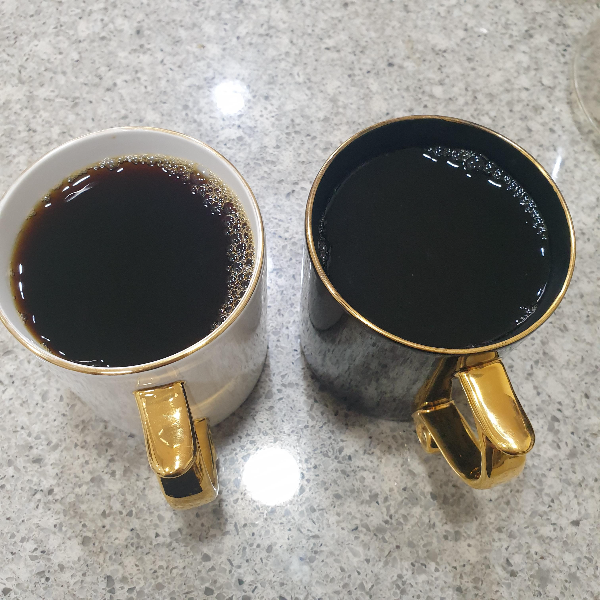 대리석 테이블 위에 흰 컵, 검은색 컵 하나씩 있다. 각 컵에는 커피가 담겨 있다.