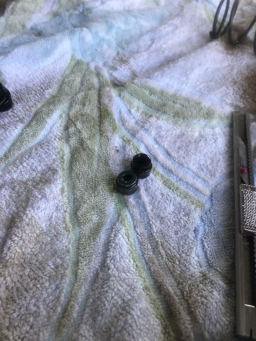 탈거된 BMW 밸브 스템씰 2개가 흰색 천 위에 놓여 있는 모습, 고무 경화와 오염 상태 확인 가능