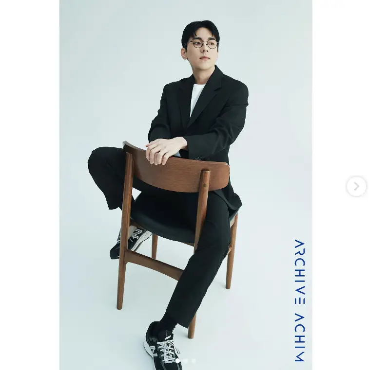 싱어게인3- 검정색 수트를 위아래로 입고 운동화를 신고 나무걸상에 앉아 옆을 보고앉아있는 58호