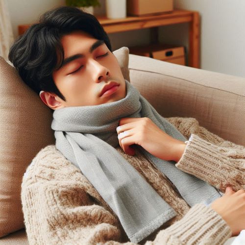 젊은 남성이 목이 아파서 목에 수건을 감고 소파에 누워 쉬고 있다.