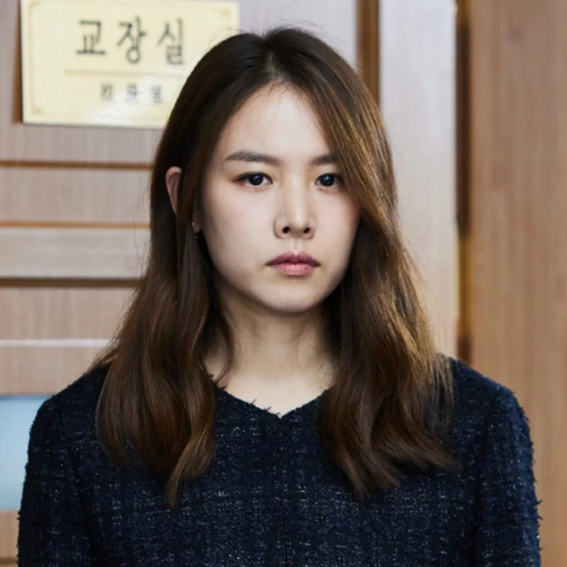 교장실 문을 배경으로 갈색 긴머리에 남색 상의를 입고 서 있는 드라마 7인의 탈출의 고명지 캐릭터