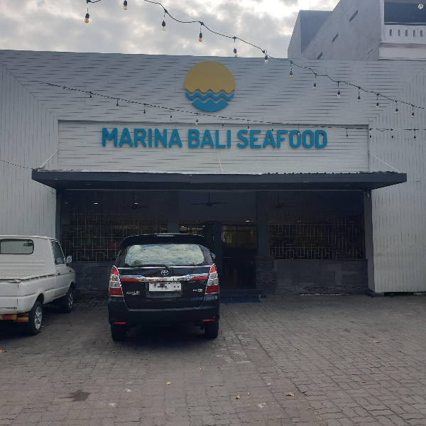 흰색 벽면에 블루 색 간판 MARINA BALI SEAFOOD라고 쓰여있다. 매장 앞 차 두 대가 주차하고 있다.