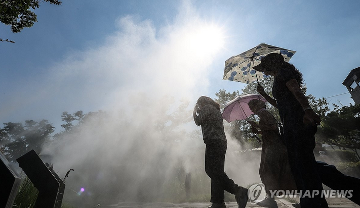 대구 지역에 폭염주의보가 발효된 18일 대구 중구 김광석다시그리기길 인근에 설치된 쿨링포그(안개형 냉각수)에서 시민들이 양산을 쓰고 더위를 피하며 이동하고 있다.