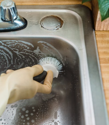 브러시로 싱크대 배수구 주변을 청소하는 모습