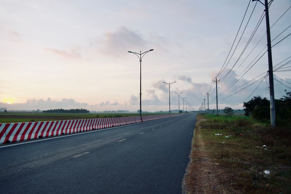 Empty highway at sunrise with power lines and open fields, capturing peaceful morning light.