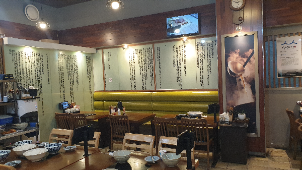 긴 액자들이 벽면에 있고 앞쪽으로는 테이블과 의자가 놓여있다.