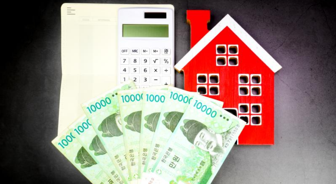 만원지폐 여러장과 집 모형, 통장 한개와 계산기 한개가 놓여있다.