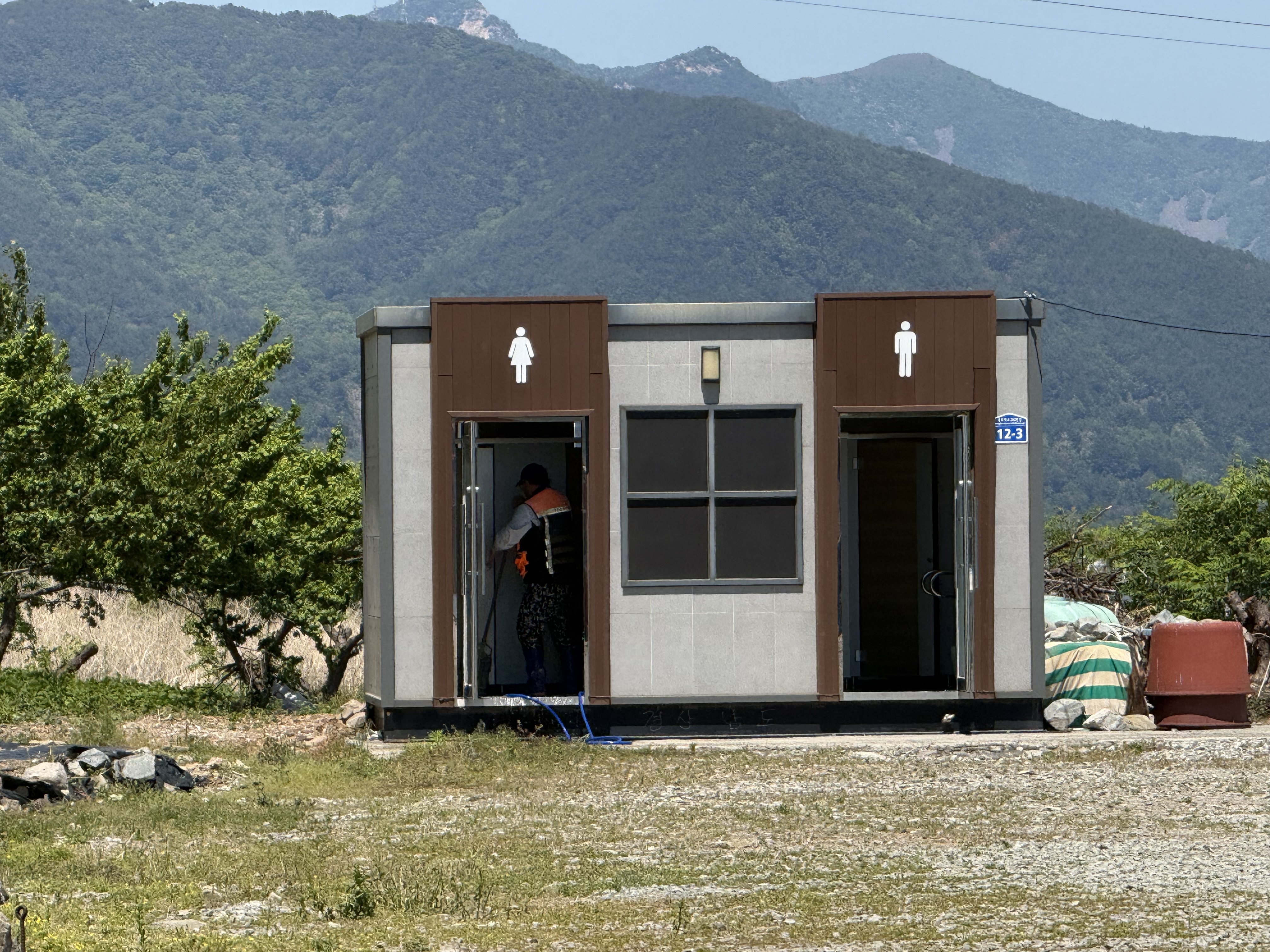 푸른 산을 배경으로 깨끗하게 관리되는 현대적인 남녀 공용 화장실 건물의 모습입니다.