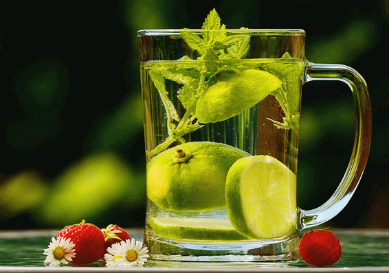 투명 유리잔에 찬물이 가득하다. 물 안에는 허브잎과 라임 조각들이 있다.