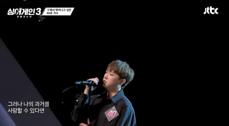 싱어게인3-
검은배경의 무대 검은색 셔츠에 검은색 스탠딩마이클 오른손으로 잡고 눈감고 노래하는 50호의 왼쪽모습