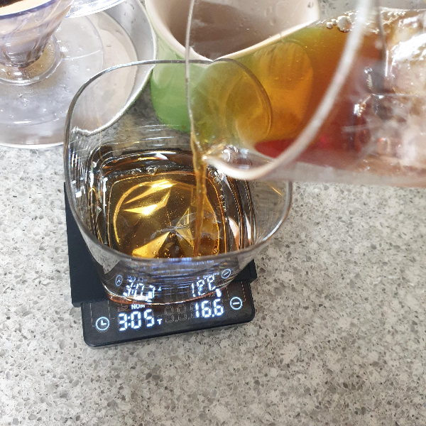 얼음이 담긴 비이커 속 커피를 거울 위에 올려진 유리잔에 붓는다.